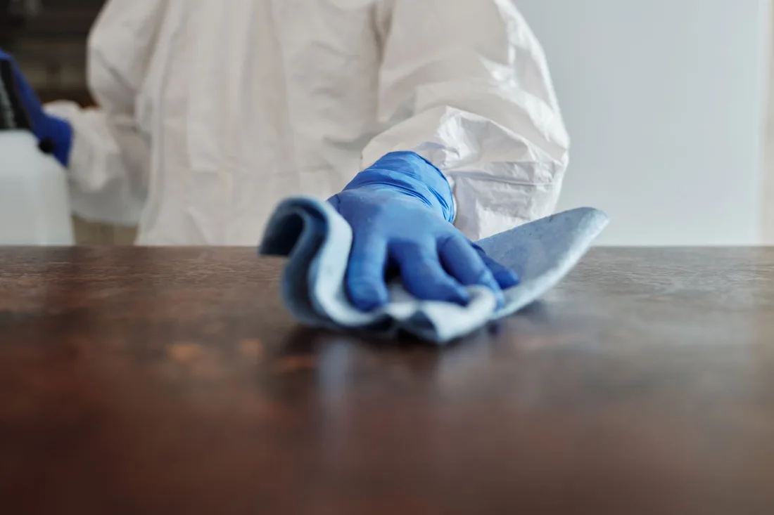 A cleaner in gloves spraying and wiping a desk surface